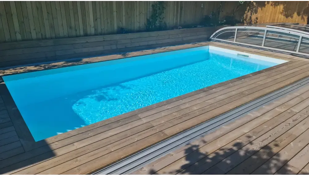 Rektangulär pool med klart blått vatten, trädeck och glasöverdrag för Pooltak Nivo Kit 1060B