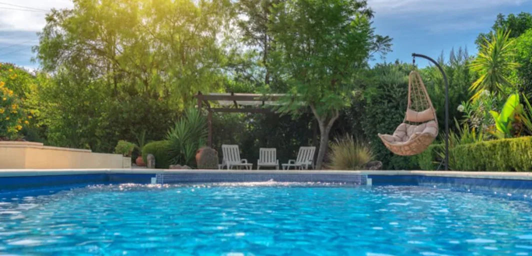 Hängande rottingfåtölj med beige kudde vid pool i grönska