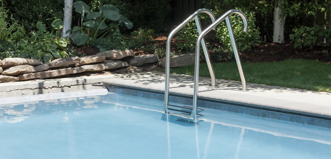 Rostfri poolstege med böjda ränder och trappsteg vid klar blå poolkant.