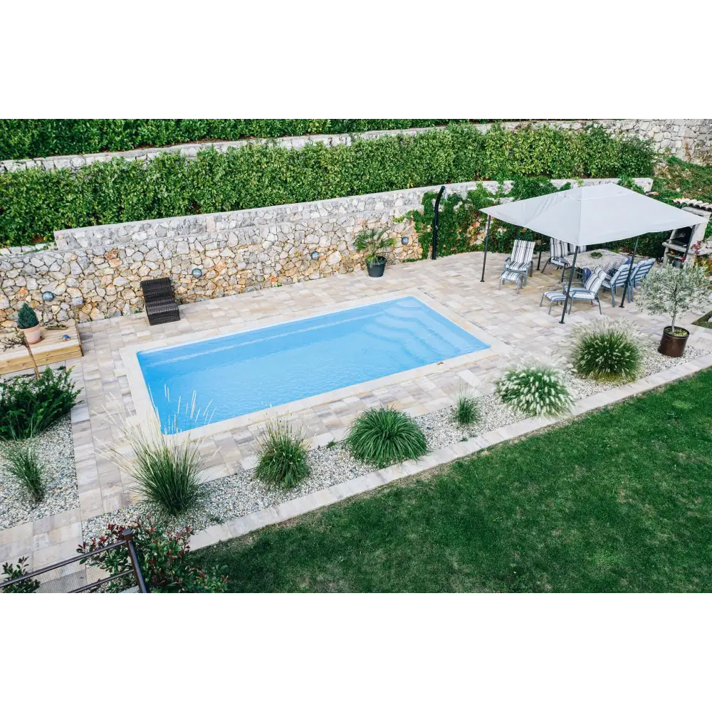 Blå rektangulär glasfiberpool Aruba med kaklad omgivning och grönskande bord