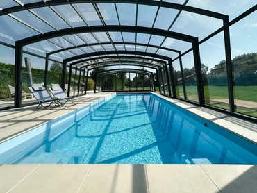 Bahama garden pool with a transparent enclosure – elongated shape, rectangular shape, indoors, clear blue water, black frame, roof with clear panels