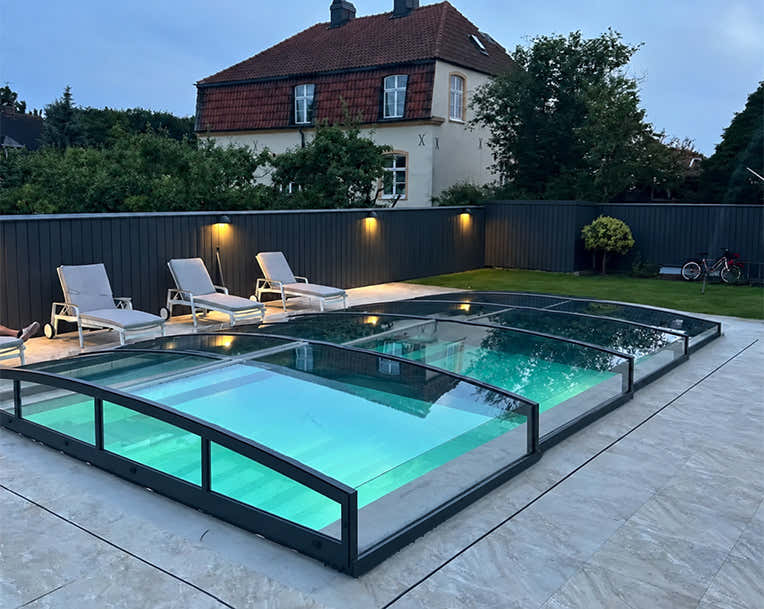 ICON KIT CLEAR pool enclosure with clear polycarbonate panels and anthracite profiles – lifestyle image of the model range.