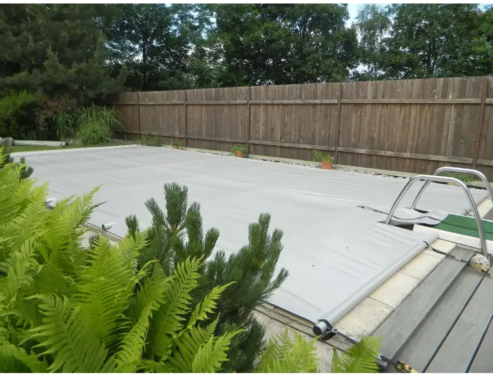 Grey pool cover including a manual operating unit – metal frame, green plants in the foreground
