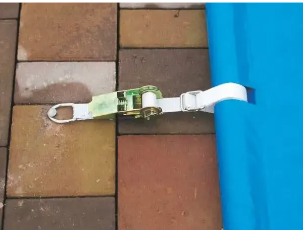 White webbing strap for a blue pool cover including a manual operating unit – green and silver tensioning mechanism