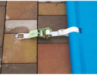 White webbing strap for a blue pool cover including a manual operating unit – green and silver tensioning mechanism
